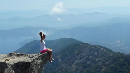 Woman with arms raised on cliff against mountains