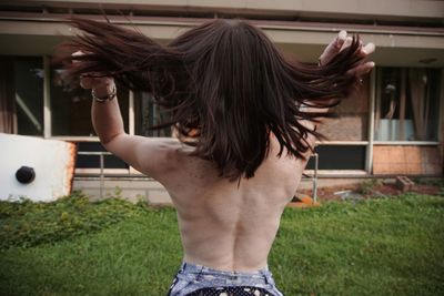 Rear view of woman playing with hair at yard