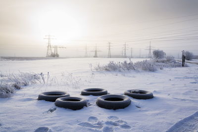 Snow covered land and electricity pylon on field against sky