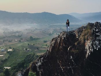 Woman standing on cliff against landscape