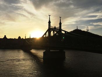 Silhouette bridge over river against sky during sunset