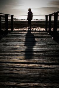 Rear view of silhouette man standing on pier over sea