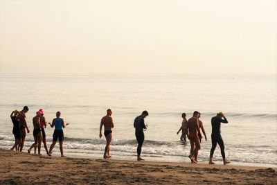 Swimmers walking at beach against clear sky