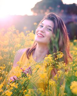 Portrait of smiling young woman with yellow flowers on field