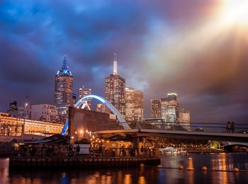 Illuminated buildings by river against sky in city