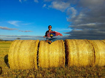 Portrait of young woman sitting on hay bales in field