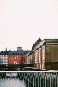 Bridge over river by buildings against clear sky