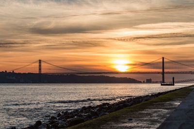 View of suspension bridge over river against cloudy sky