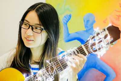 Young woman playing guitar with illuminated string lights at home