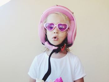 Portrait of cute girl in sunglasses wearing helmet against wall