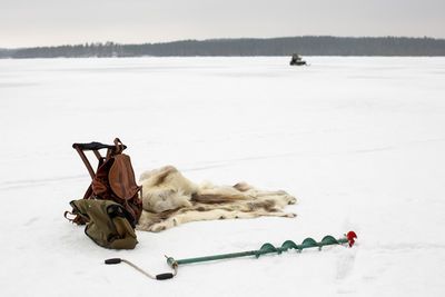 Backpack kept by animal skin and ice auger on snow in winter