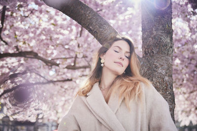 Young woman standing under cherry blossom