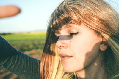 Close-up of young woman shielding eyes while standing at field against sky on sunny day