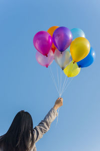 Low angle view of mid adult woman holding colorful balloons while standing against clear blue sky