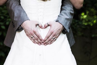 Midsection of bridegroom making heart shape with hands on bride back at yard