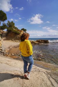 Rear view of woman walking on beach against sky