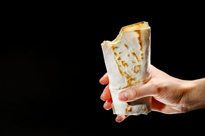 Cropped hand holding ice cream cone against black background
