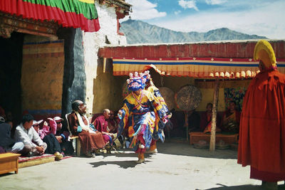 People looking at performers in traditional costume dancing outside temple during festival