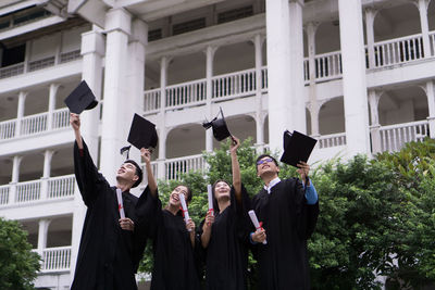 Students in university gowns throwing mortarboards while standing against building