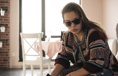 Young woman wearing sunglasses sitting at home