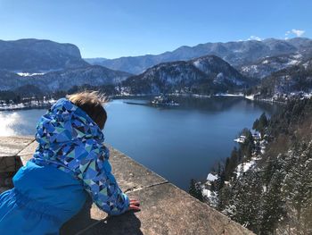 Side view of boy standing on retaining wall by lake against sky during winter