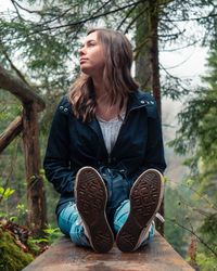 Young woman looking away while sitting on bench in forest