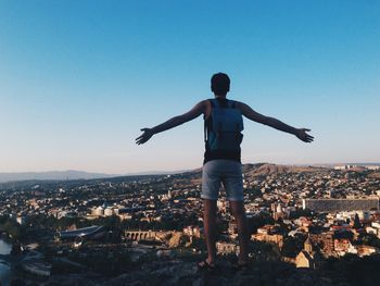 Rear view of man standing with arms outstretched against cityscape