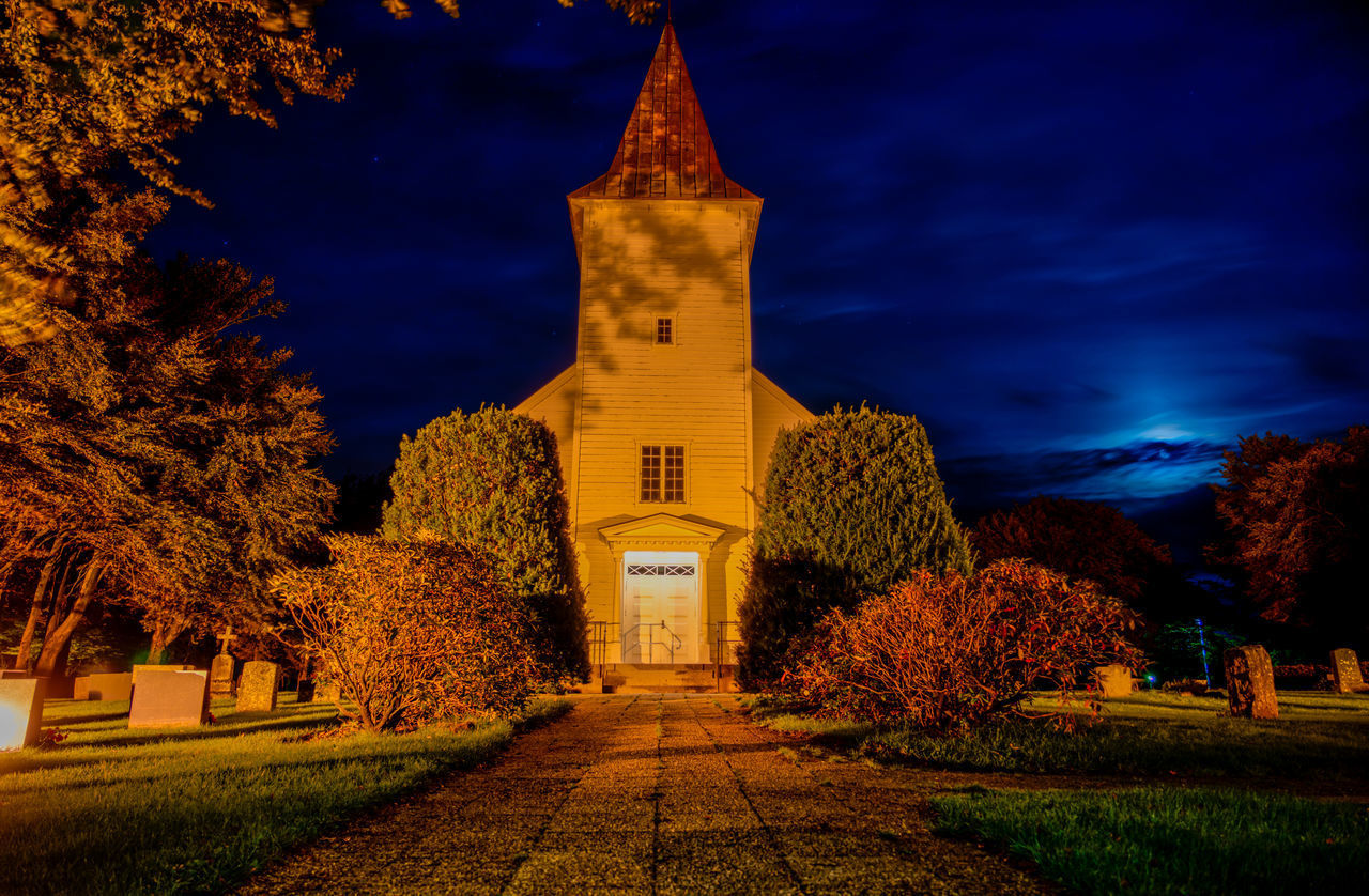 ILLUMINATED BUILDING BY TREES AT NIGHT