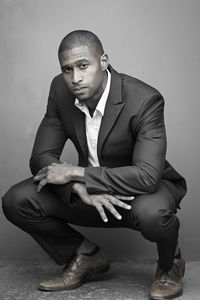 Portrait of businessman wearing blazer crouching against wall