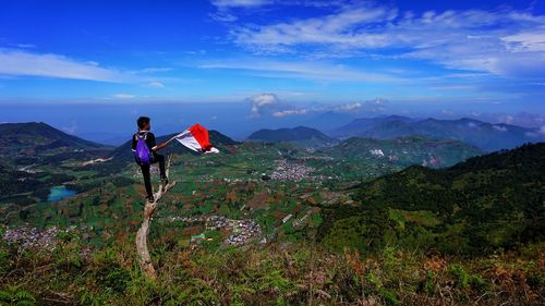 Rear view of man holding indonesian flag while standing tree trunk