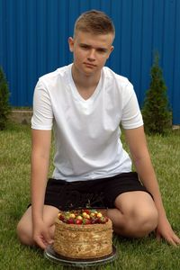 Teenager with a cake in his hands sitting on the green grass