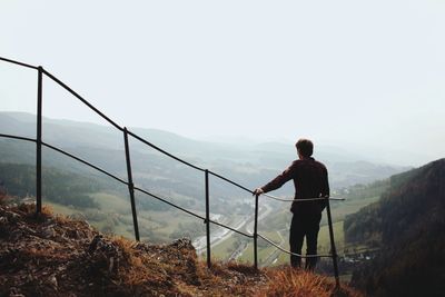 Rear view of man standing on mountain against sky