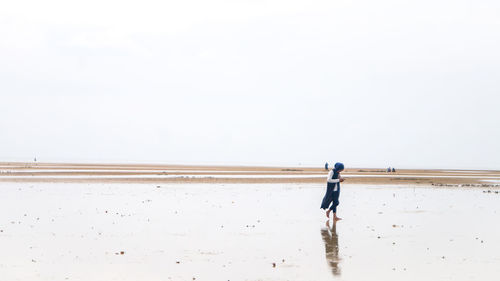 Rear view of man walking on beach against clear sky