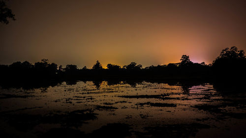 Silhouette trees by lake against sky during sunset