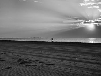 Man walking on shore at beach against sky