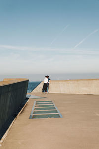 People looking at sea standing against sky