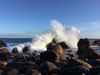 Waves splashing on rocks at shore against sky