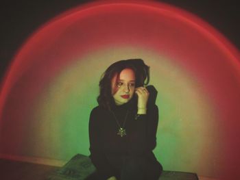 Portrait of young woman standing against illuminated wall