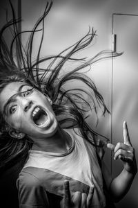 Portrait of girl tossing hair screaming while standing against wall