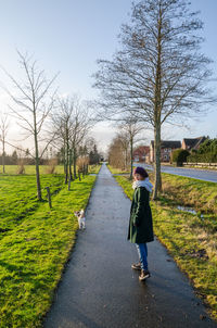 Rear view of women walking with dog on footpath with bare trees during winter