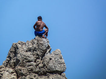 Low angle view of woman standing on rock against clear blue sky