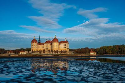 Buildings at waterfront against cloudy sky