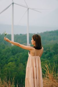 Woman with arms raised standing on field against sky