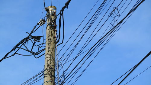 Low angle view of electricity pylon against blue sky
