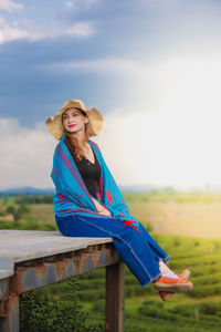 Young woman sitting on field against sky