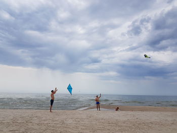 People flying kite on beach against sky