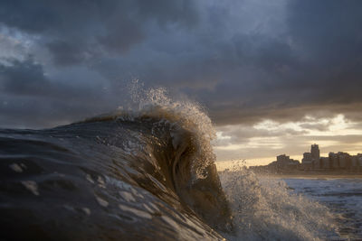 Sea waves splashing against cloudy sky during sunset