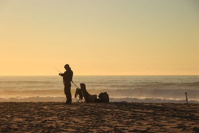 Silhouette people on beach against sky during sunset