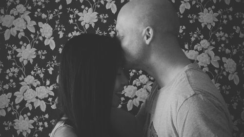 Close-up of man kissing forehead of woman against wall