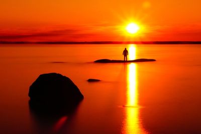 Silhouette person on sea against orange sky during sunset